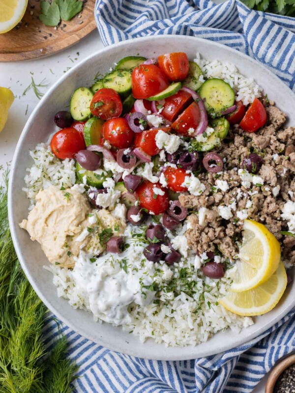 Greek turkey, cucumber-tomato salad, and other toppings are served on a bed of rice with a lemon wedge.