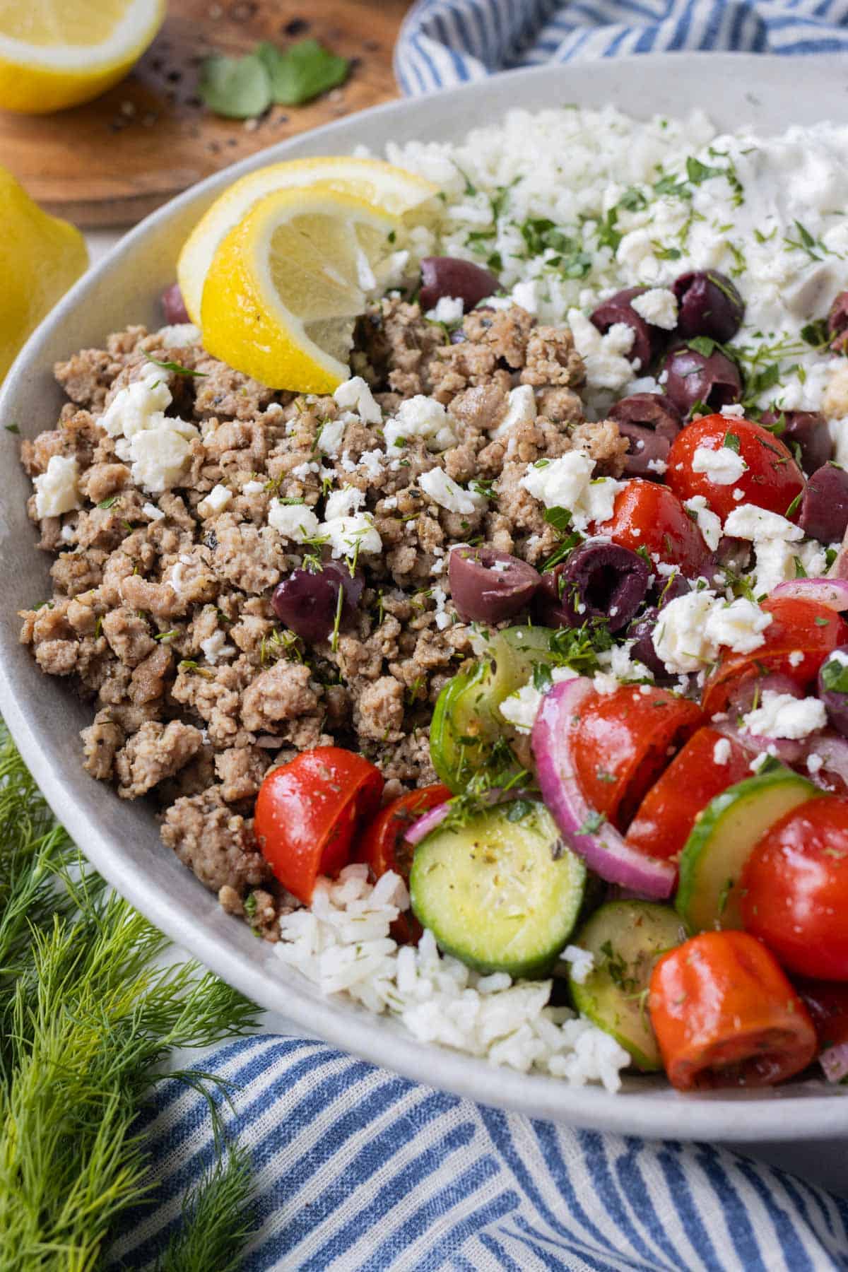 Greek turkey, cucumber-tomato salad, and other toppings are served on a bed of rice with a lemon wedge.