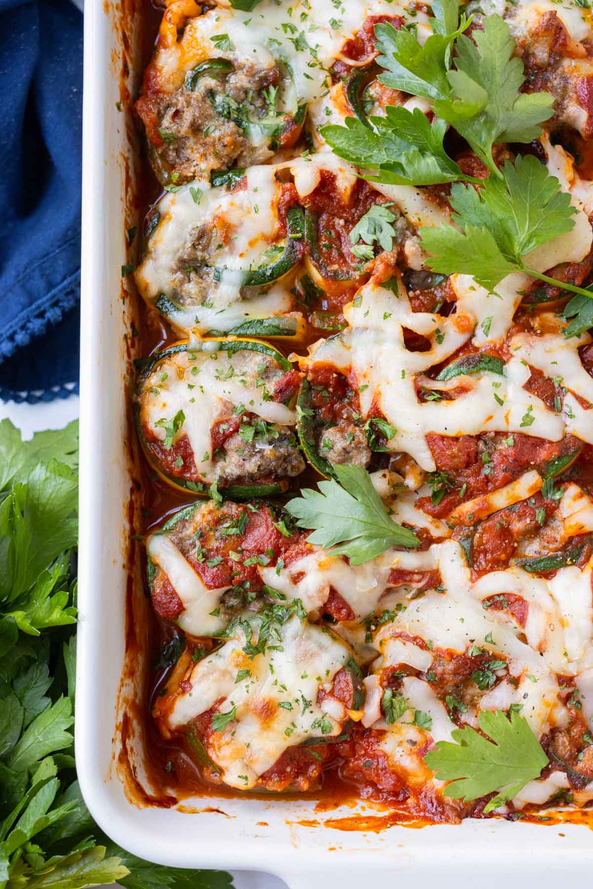 Low-carb and keto zucchini lasagna roll-ups in a white baking dish with mozzarella and marinara sauce.