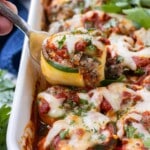 A zucchini lasagna roll-up being lifted from a white baking dish.