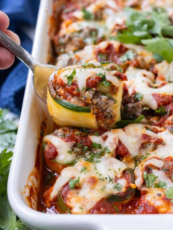 A zucchini lasagna roll-up being lifted from a white baking dish.