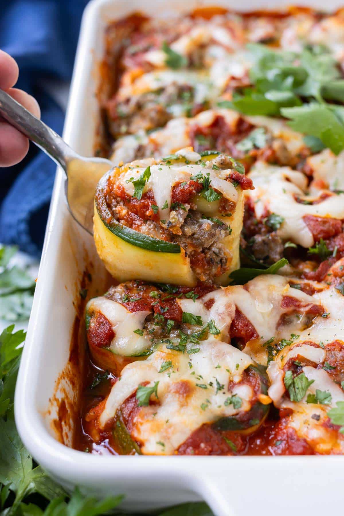 A zucchini lasagna roll-up being lifted from a white baking dish.