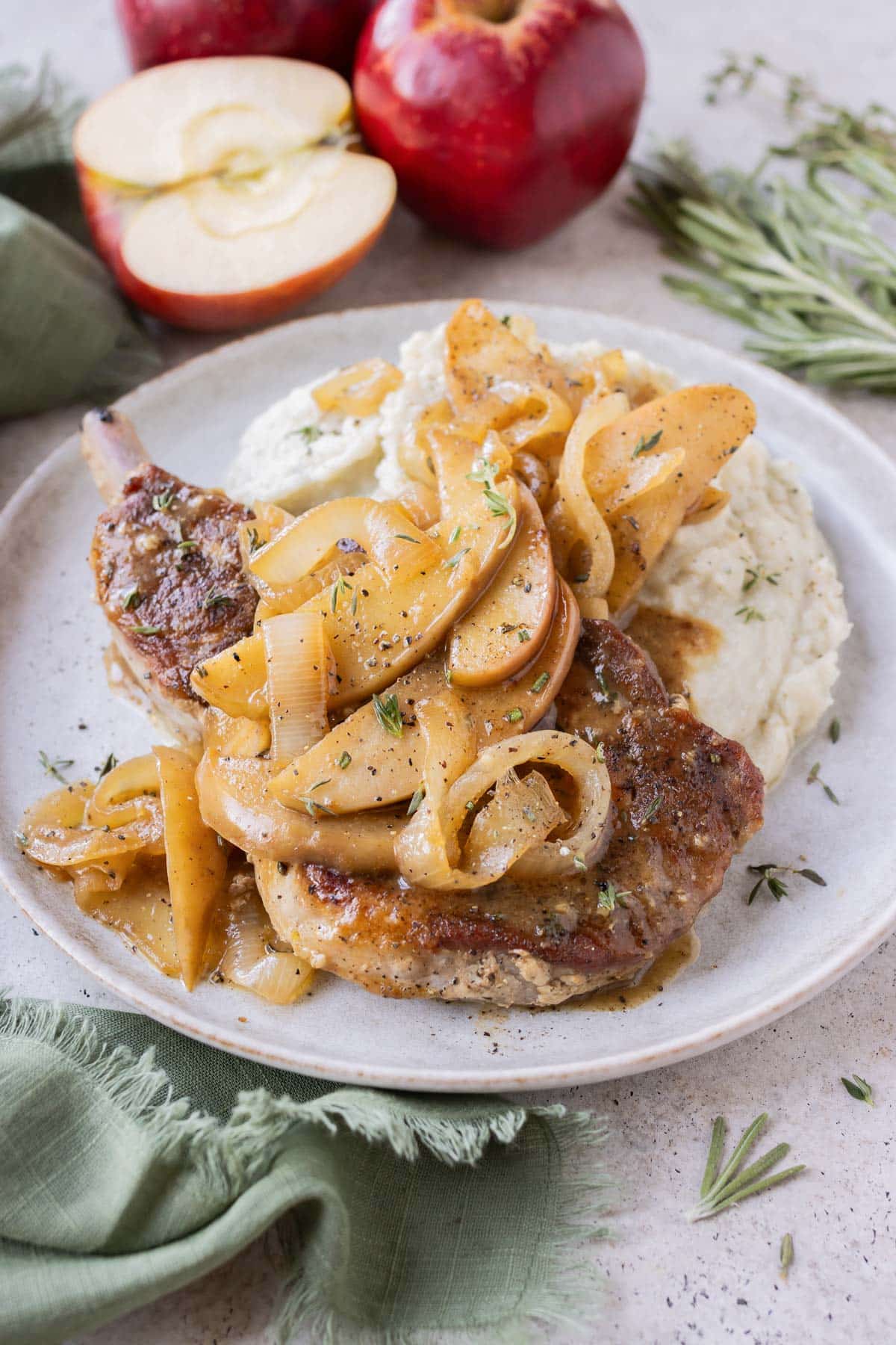 Bone in pork chops, apples, and onions are served on a white plate with mashed potatoes.