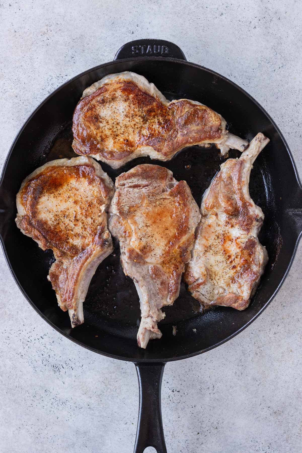 Pork chops are cooked in a cast iron skillet.