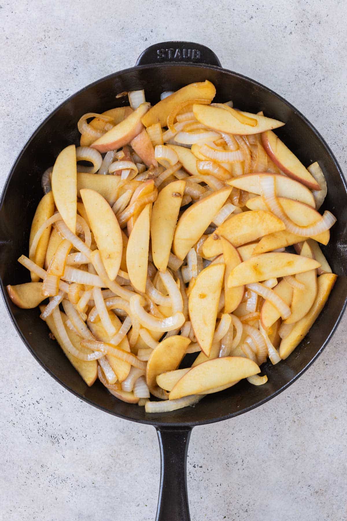 Apples and onions are cooked in a cast iron skillet.