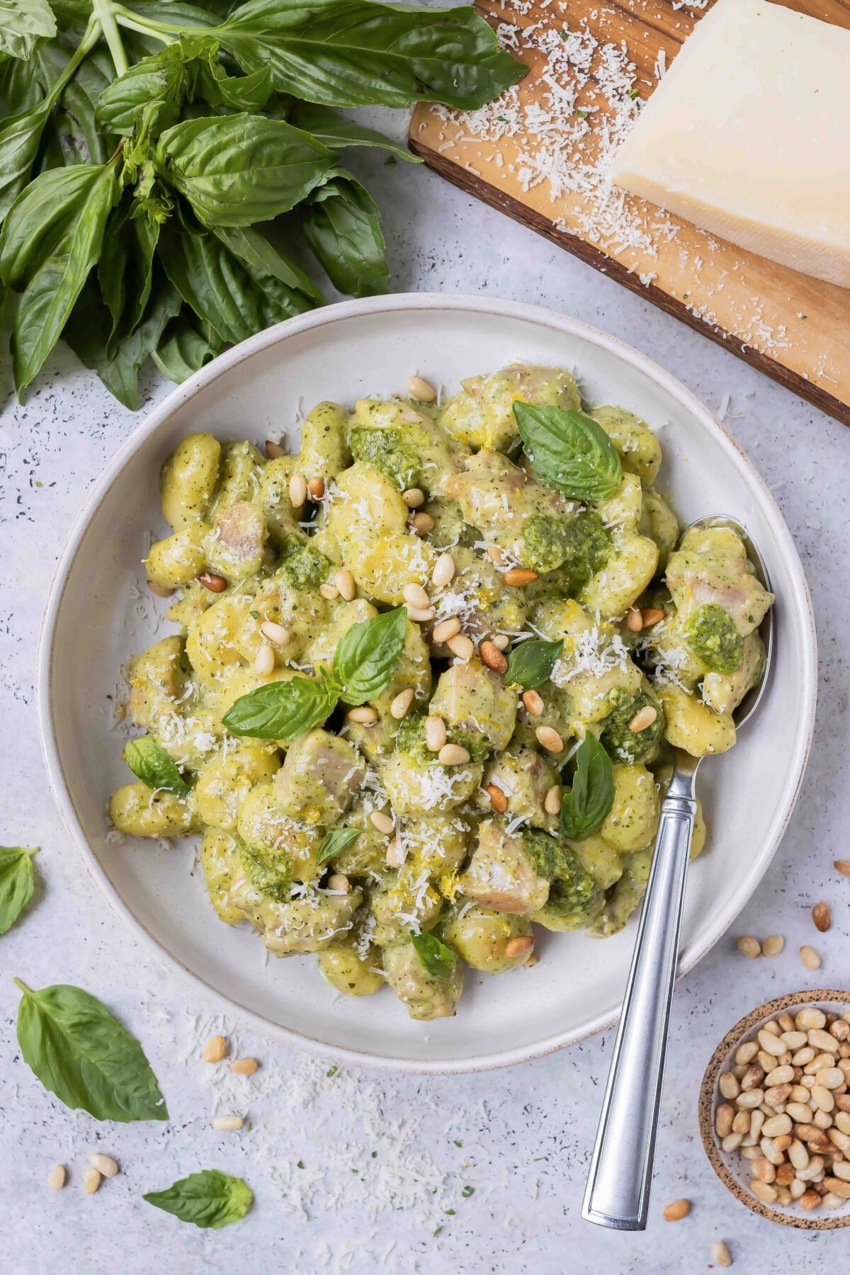 A white bowl is full of chicken and gnocchi in a creamy pesto sauce.