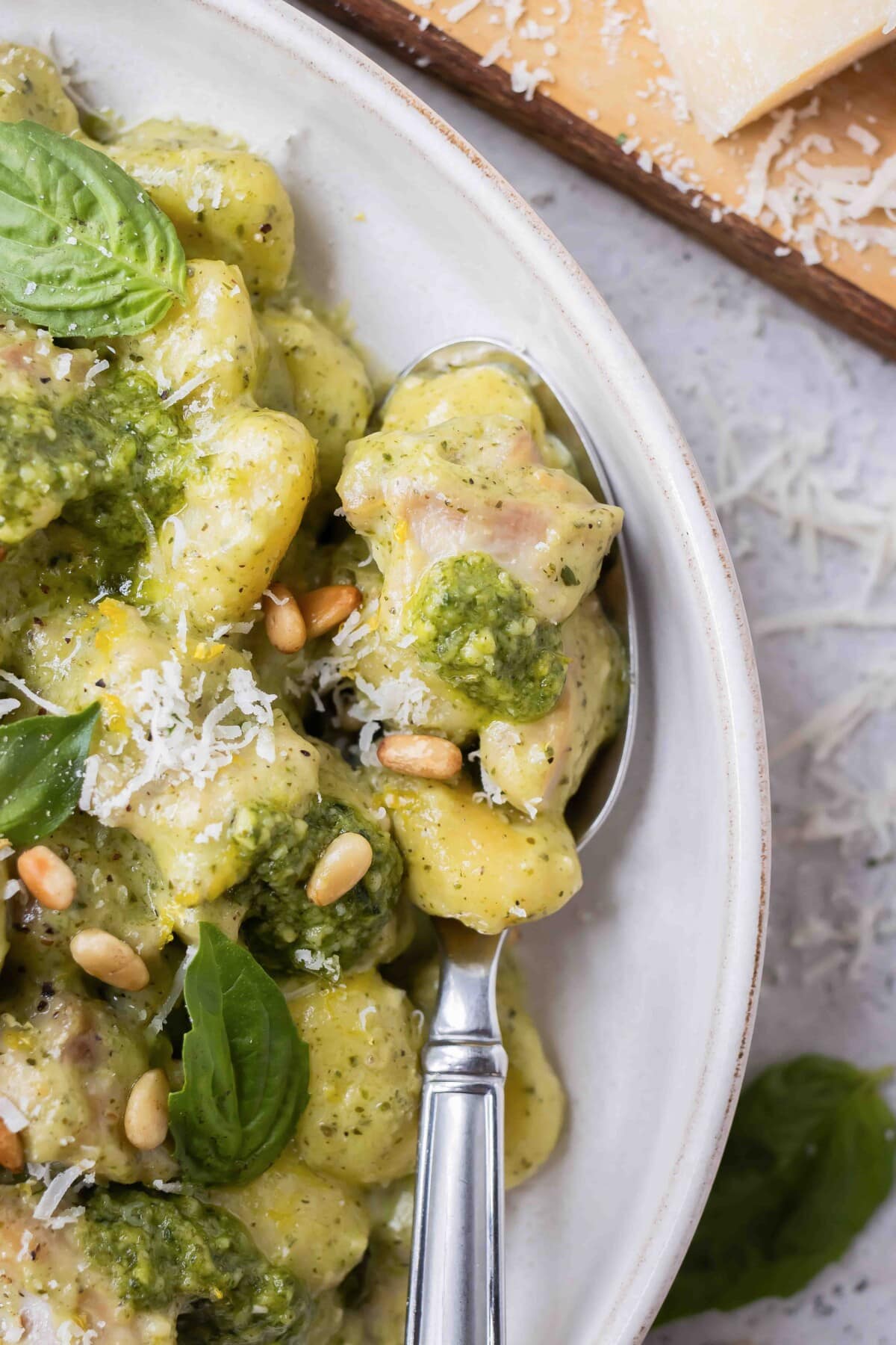 A spoon is scooping up a bite of pesto gnocchi with chicken.