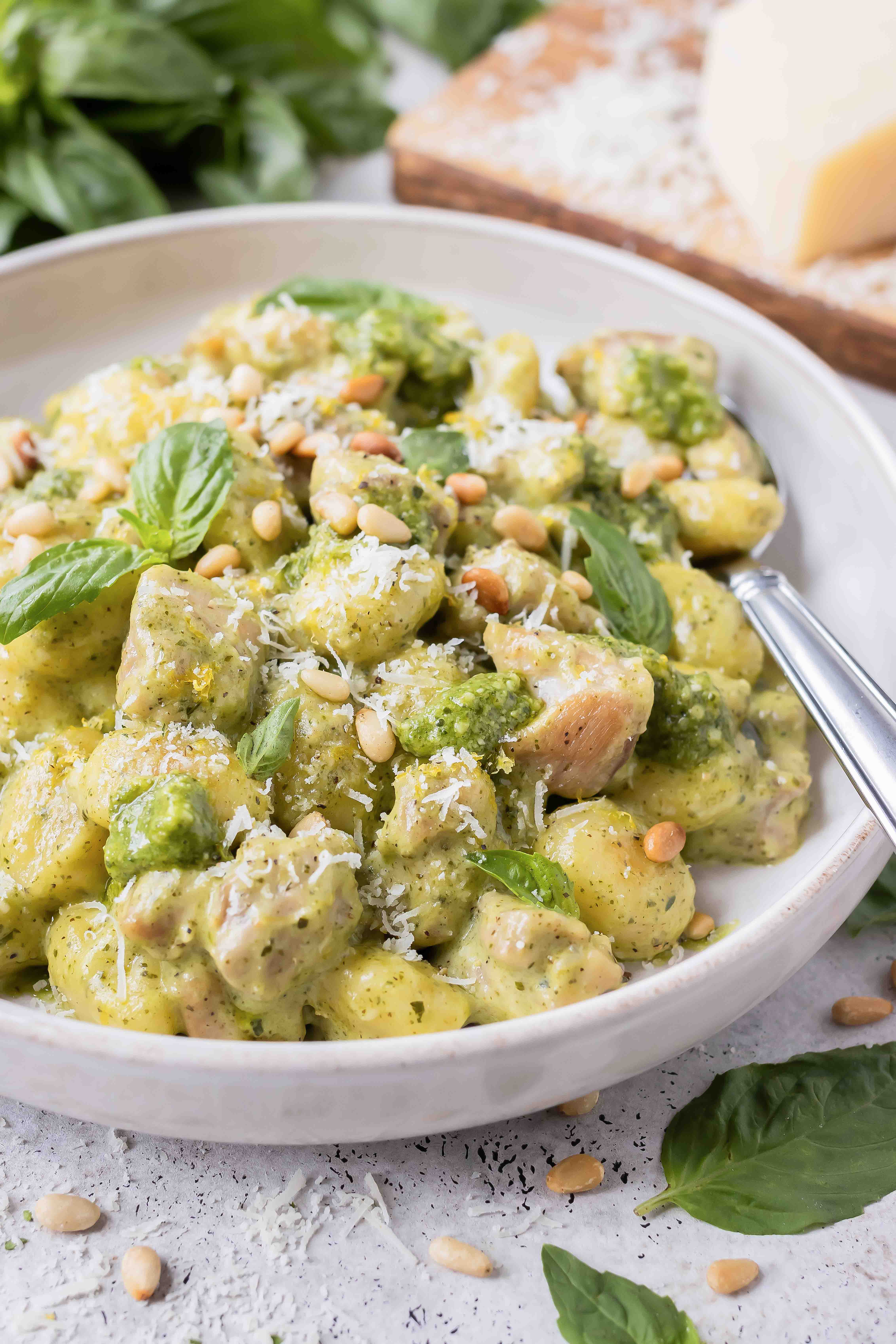 Creamy pesto chicken gnocchi is in a white bowl with basil leaves.