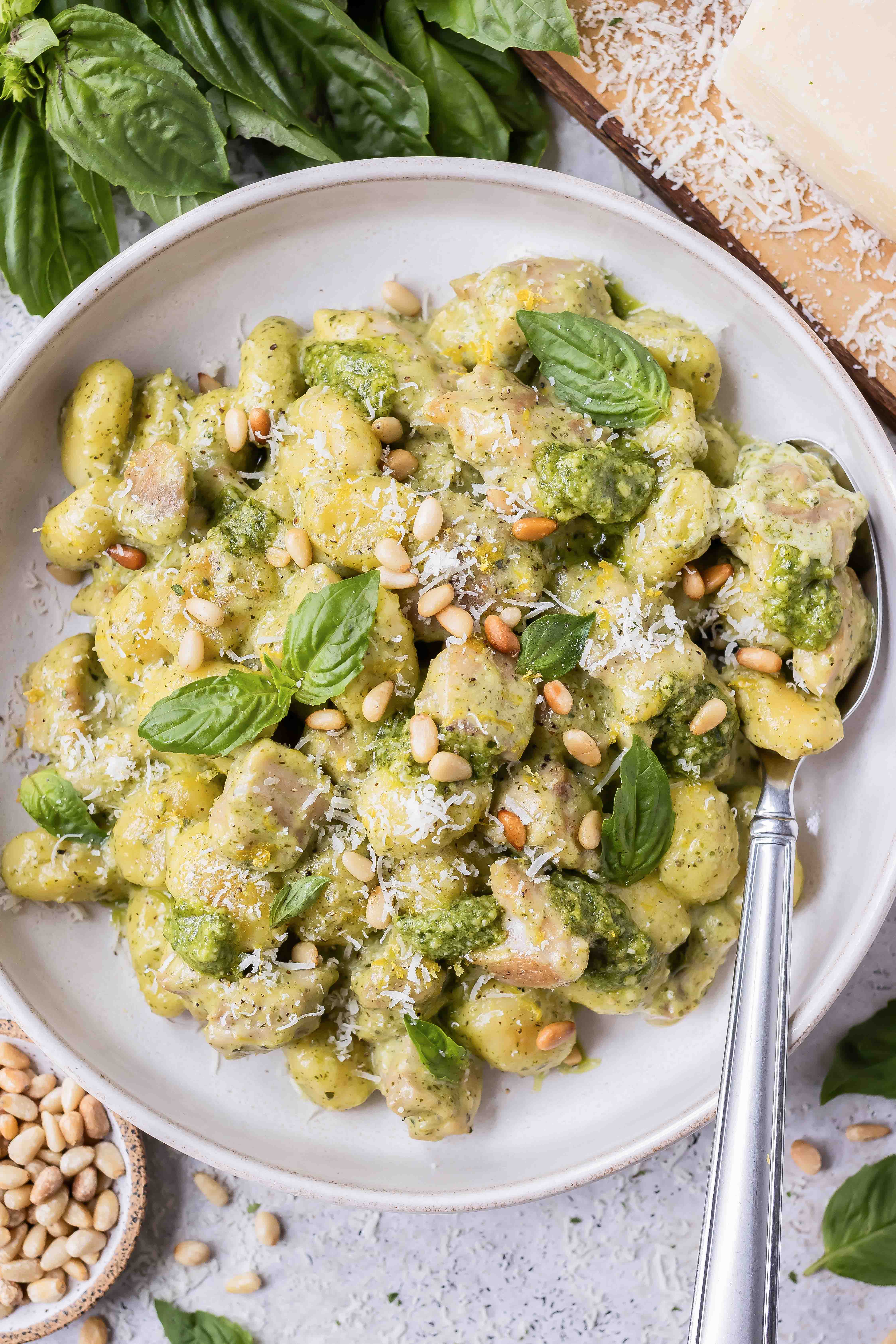 Creamy pesto gnocchi with chicken is in a bowl with a serving spoon.