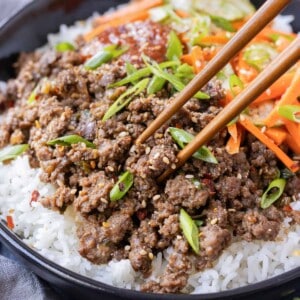 Chopsticks are picking up a bite of Korean beef from a bowl.