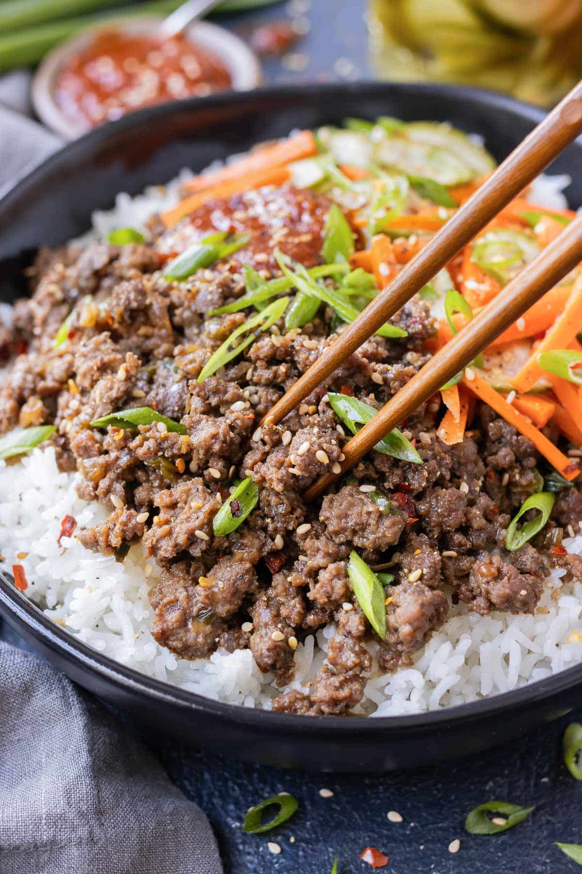 Chopsticks are picking up a bite of Korean beef from a bowl.