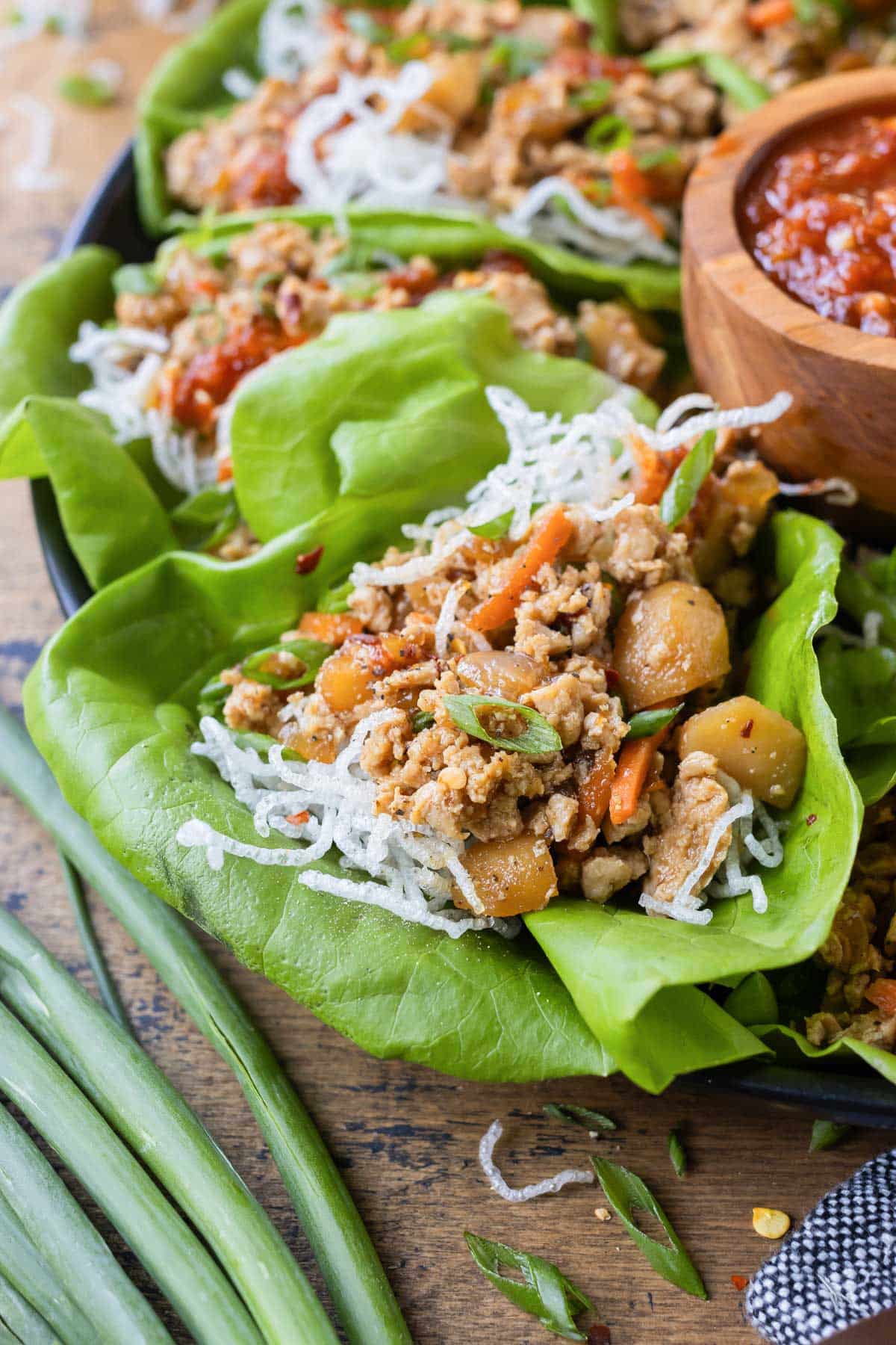 Chicken lettuce wraps are served with a dipping sauce, topped with crispy rice noodles.