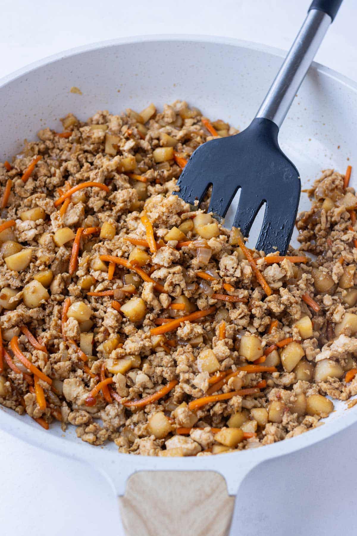 Sauce is added to the ground chicken on the stove.