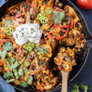 A spoon is scooping up a serving of a ground beef taco skillet recipe from a cast iron pan.