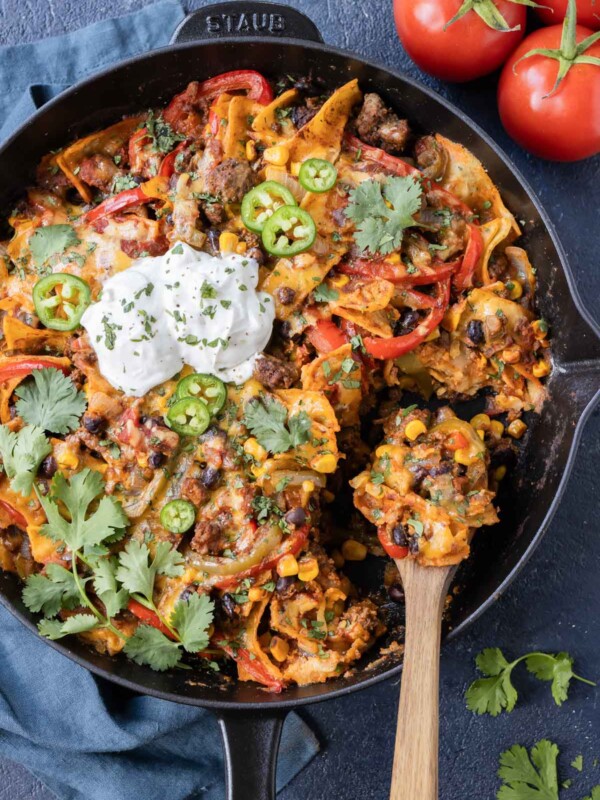 A spoon is scooping up a serving of a ground beef taco skillet recipe from a cast iron pan.