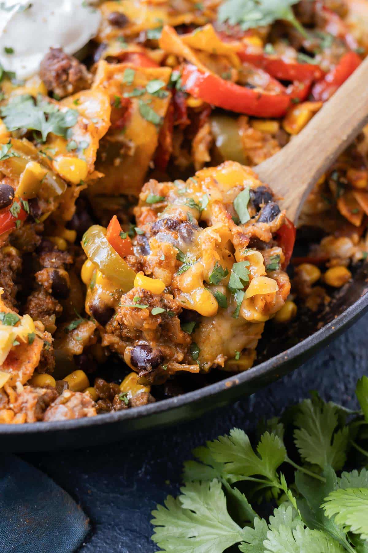 A spoon has a scoop of a cheesy beef taco from a cast iron skillet.