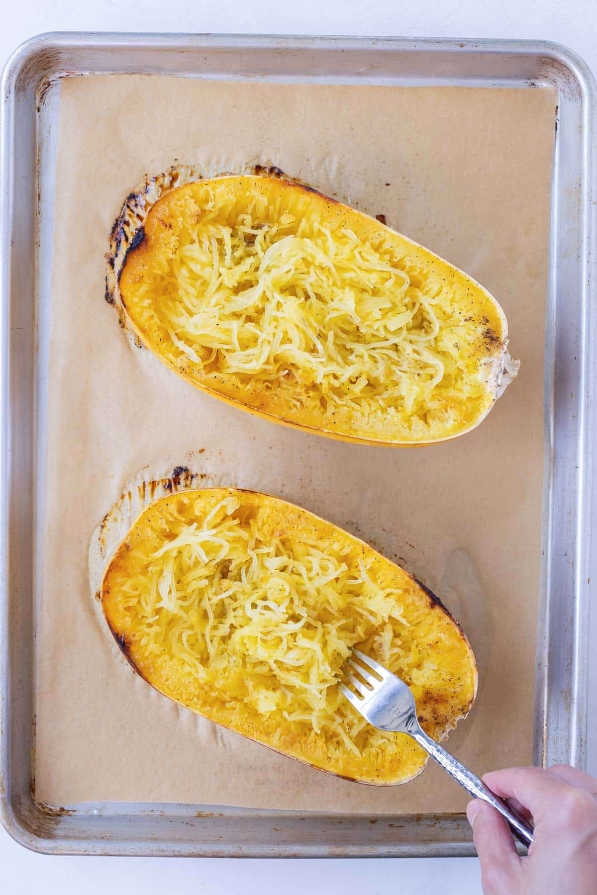 A fork is scraping the insides of a baked spaghetti squash to form into spaghetti-like strands.