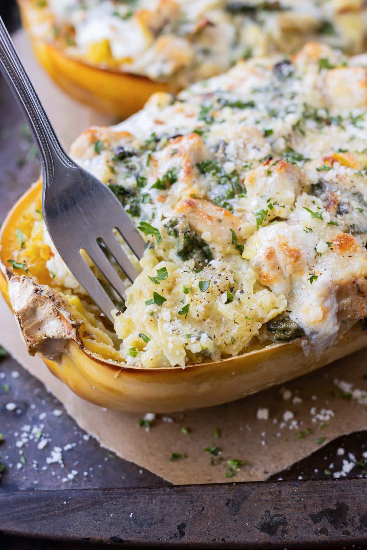 A fork digs into a baked spaghetti squash filled with a creamy spinach and artichoke filling with chicken.