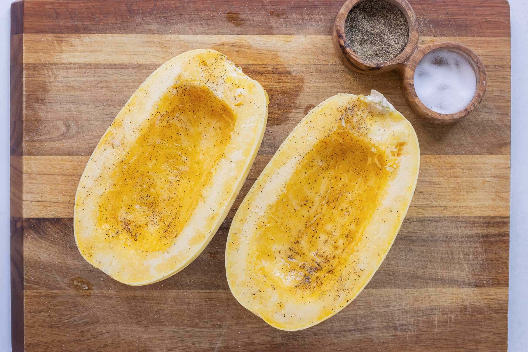 Two spaghetti squash halves that have been covered in oil, salt, and black pepper before roasting in the oven.