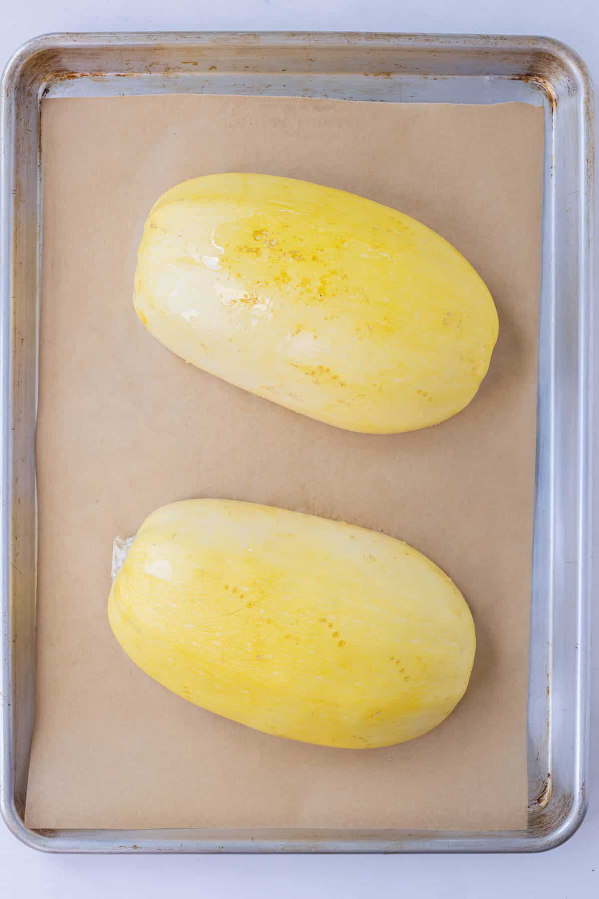 Spaghetti squash placed cut side down on a parchment paper lined baking sheet to be baked in the oven.