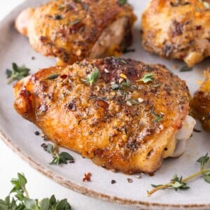 Honey mustard chicken thighs that were baked in the oven are served on a white plate with thyme.