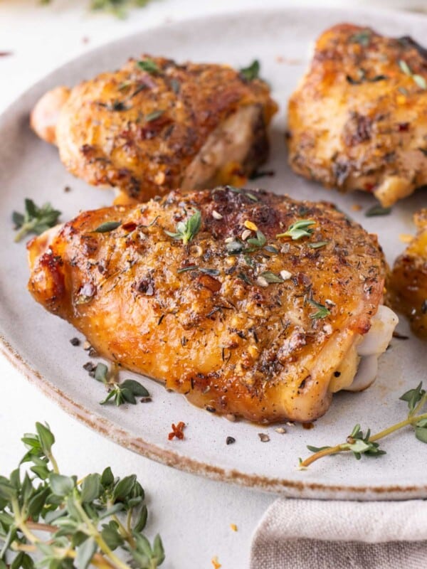 Honey mustard chicken thighs that were baked in the oven are served on a white plate with thyme.