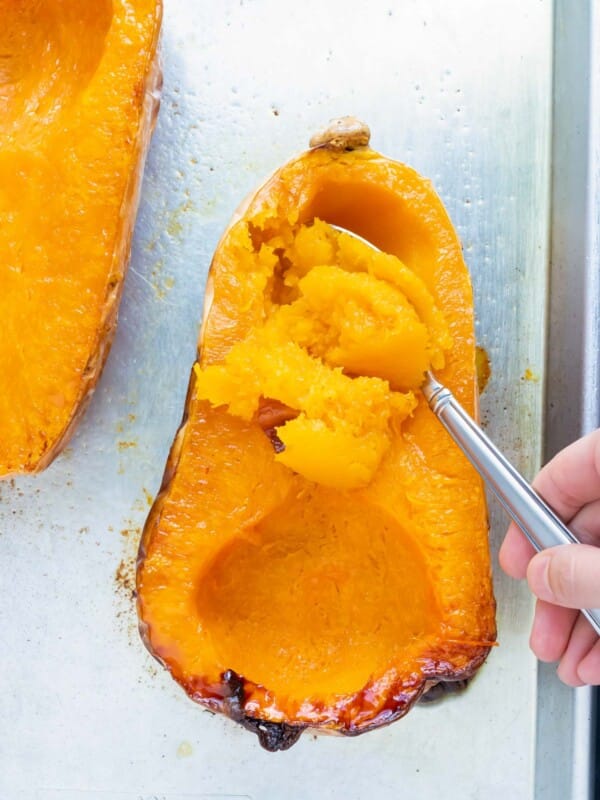 A roasted butternut squash with a spoon scooping out the flesh on a baking sheet.