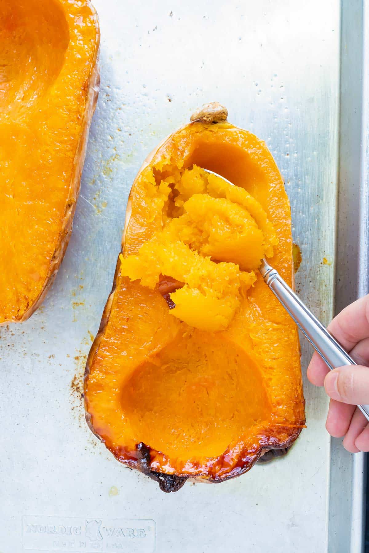 A roasted butternut squash with a spoon scooping out the flesh on a baking sheet.