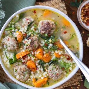 A metal spoon is shown in a bowl of healthy Italian wedding soup.