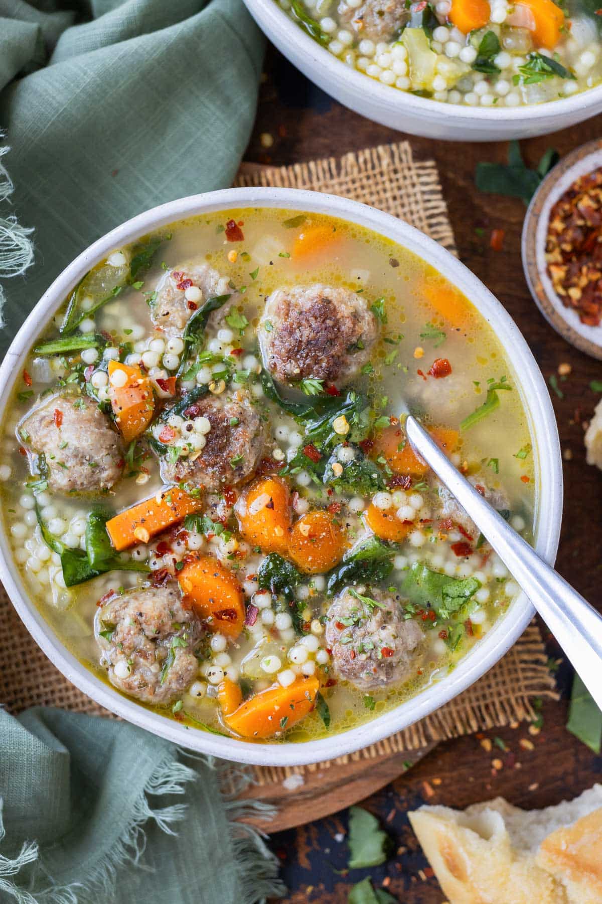 A metal spoon is shown in a bowl of healthy Italian wedding soup.