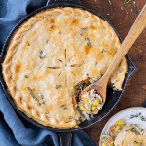 A wooden spoon scoops a serving of Skillet Chicken Pot Pie onto a plate.