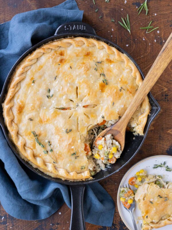 A wooden spoon scoops a serving of Skillet Chicken Pot Pie onto a plate.