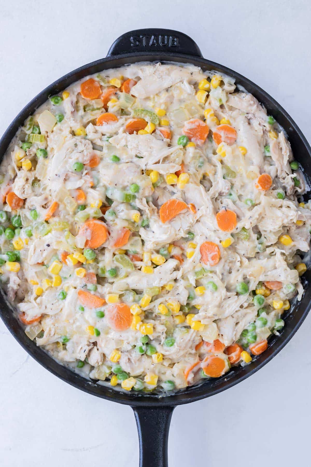 Chicken, veggies, and sauce are stirred together in a skillet.