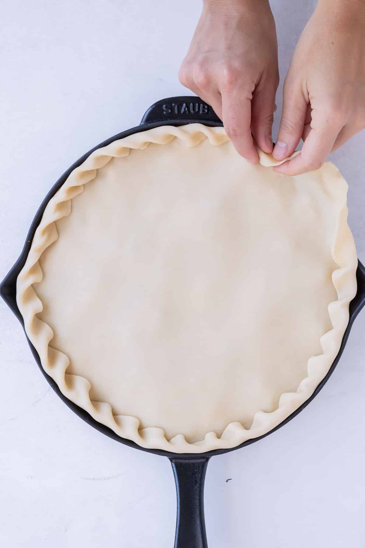 Pie crust is added on top of chicken pot pie filling in a skillet.