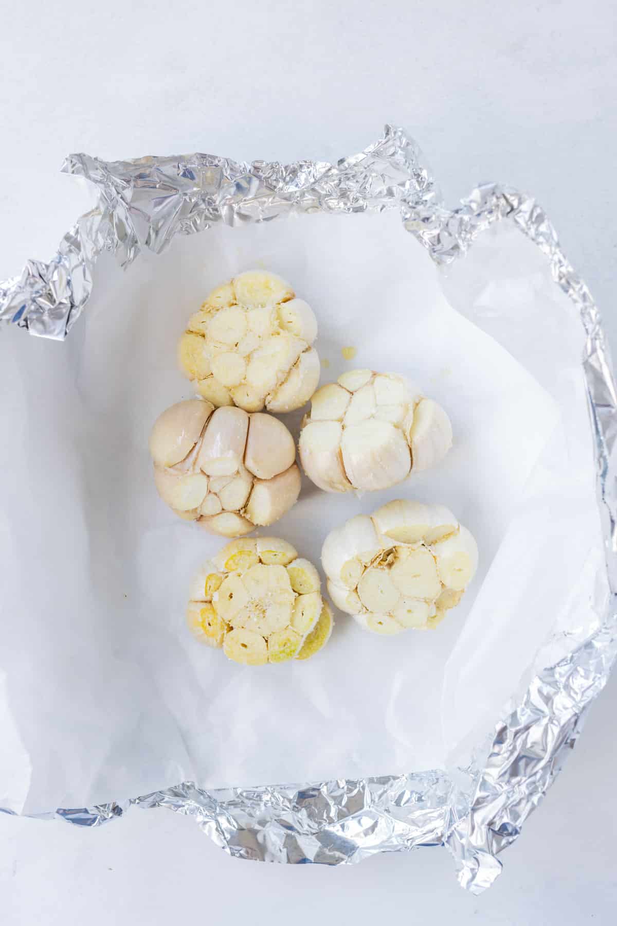 Prepped garlic is placed in a foil packet with a layer of parchment paper.