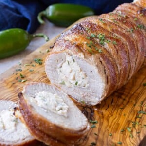 Bacon wrapped stuffed pork tenderloin is served on a wooden cutting board.