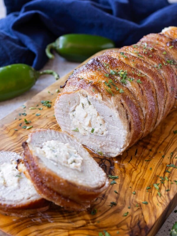 Bacon wrapped stuffed pork tenderloin is served on a wooden cutting board.