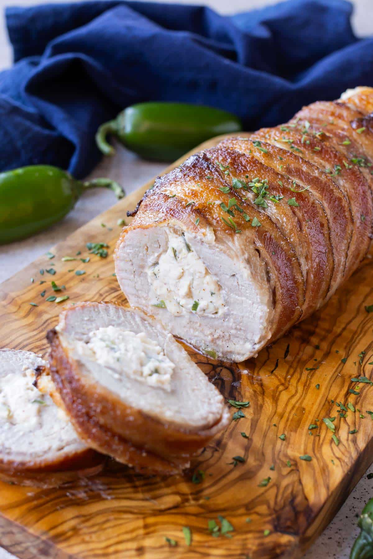 Bacon wrapped stuffed pork tenderloin is served on a wooden cutting board.