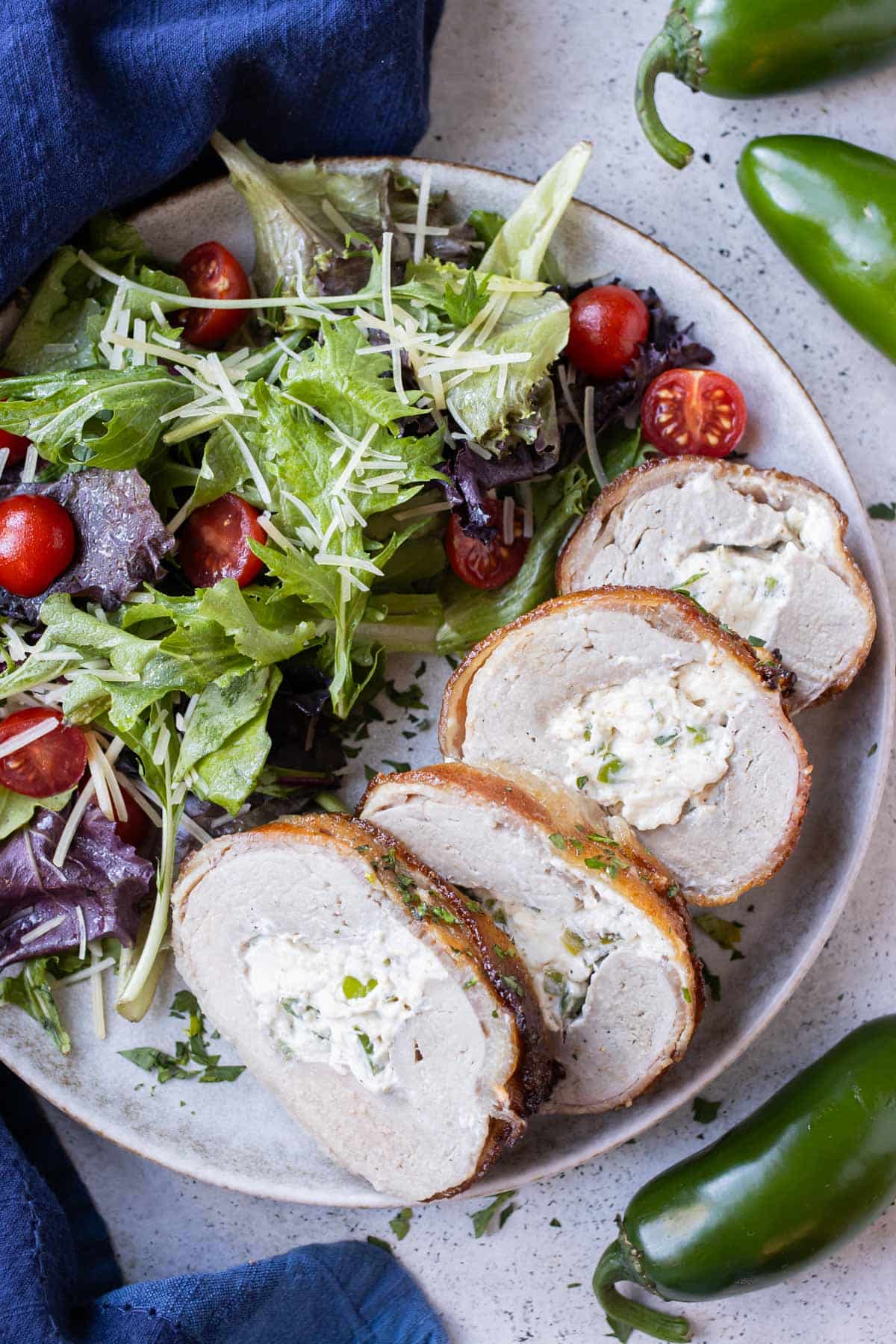 Slices of bacon wrapped stuffed pork tenderloin are served alongside a salad.