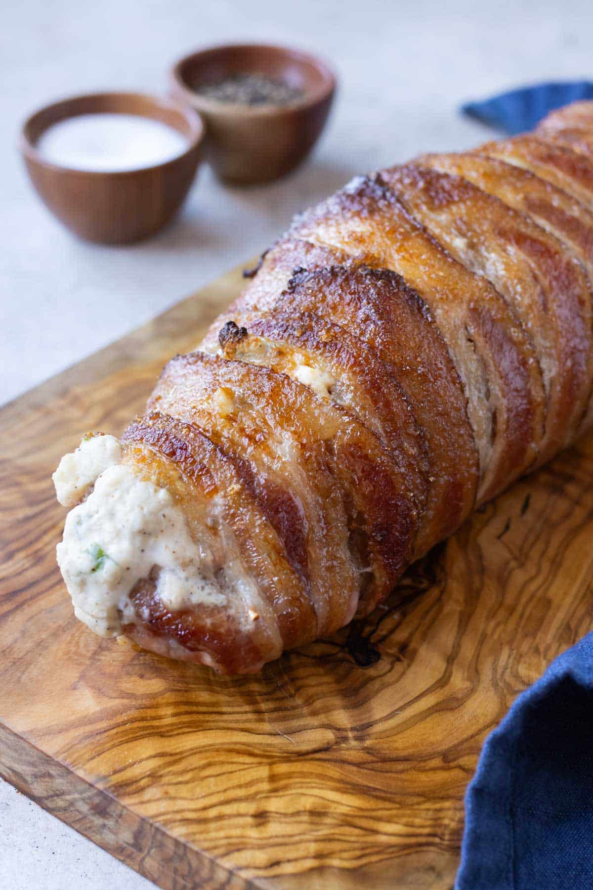 Bacon wrapped stuffed pork tenderloin is transferred to a cutting board after cooking.