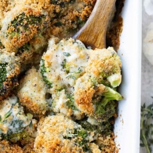 A baking dish full of a broccoli au gratin recipe with a spoon scooping it up.