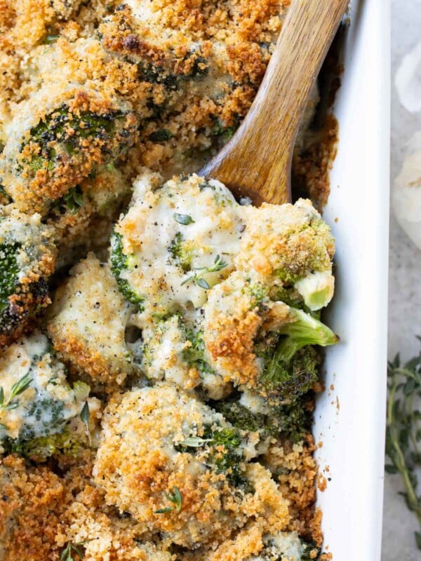 A baking dish full of a broccoli au gratin recipe with a spoon scooping it up.