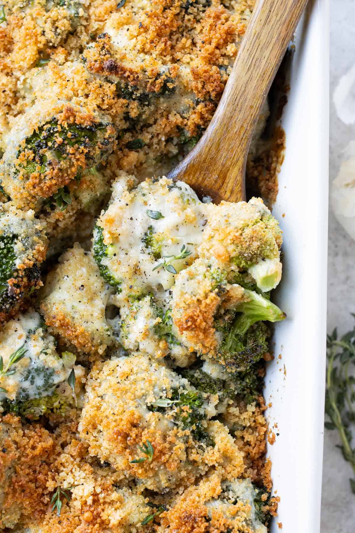 A baking dish full of a broccoli au gratin recipe with a spoon scooping it up.