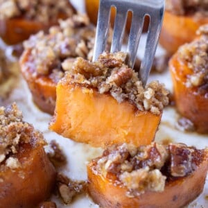 A fork is picking up a melting sweet potato with a pecan brown sugar crumble from a tray for Thanksgiving.