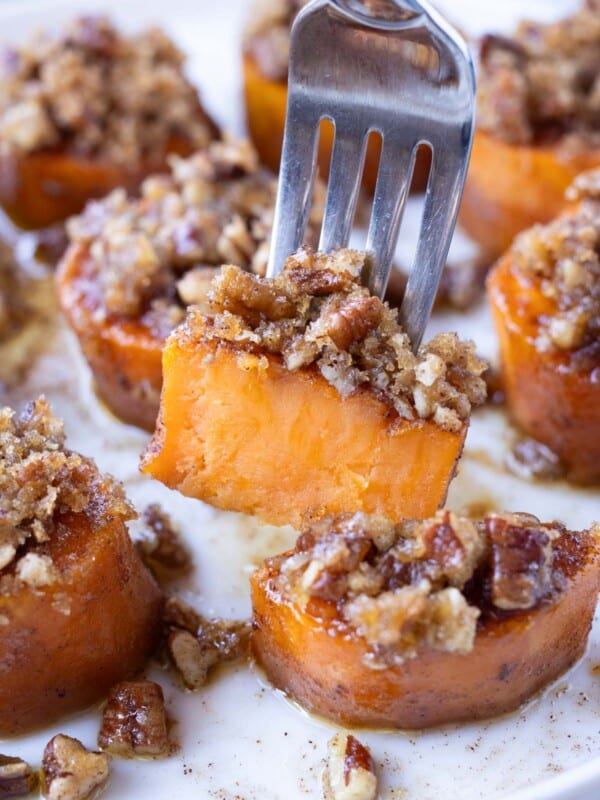 A fork is picking up a melting sweet potato with a pecan brown sugar crumble from a tray for Thanksgiving.