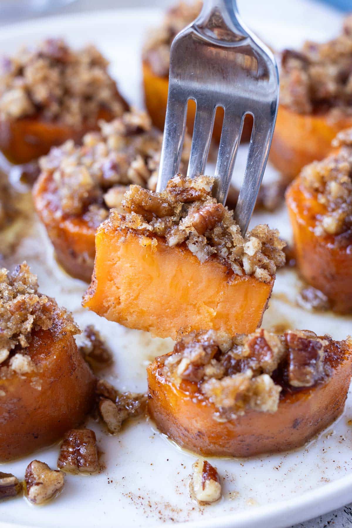 A fork is picking up a melting sweet potato with a pecan brown sugar crumble from a tray for Thanksgiving.