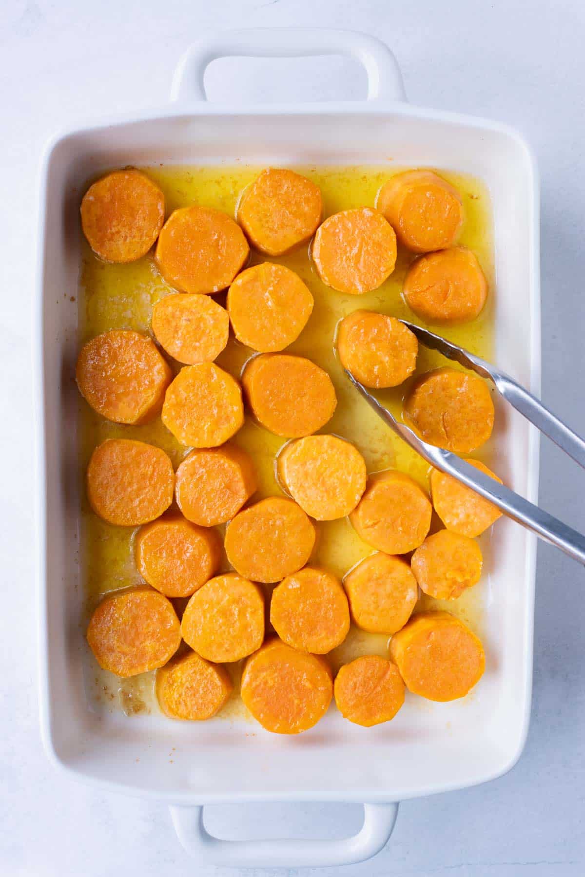 Sliced sweet potatoes are drizzled with oil before baking.