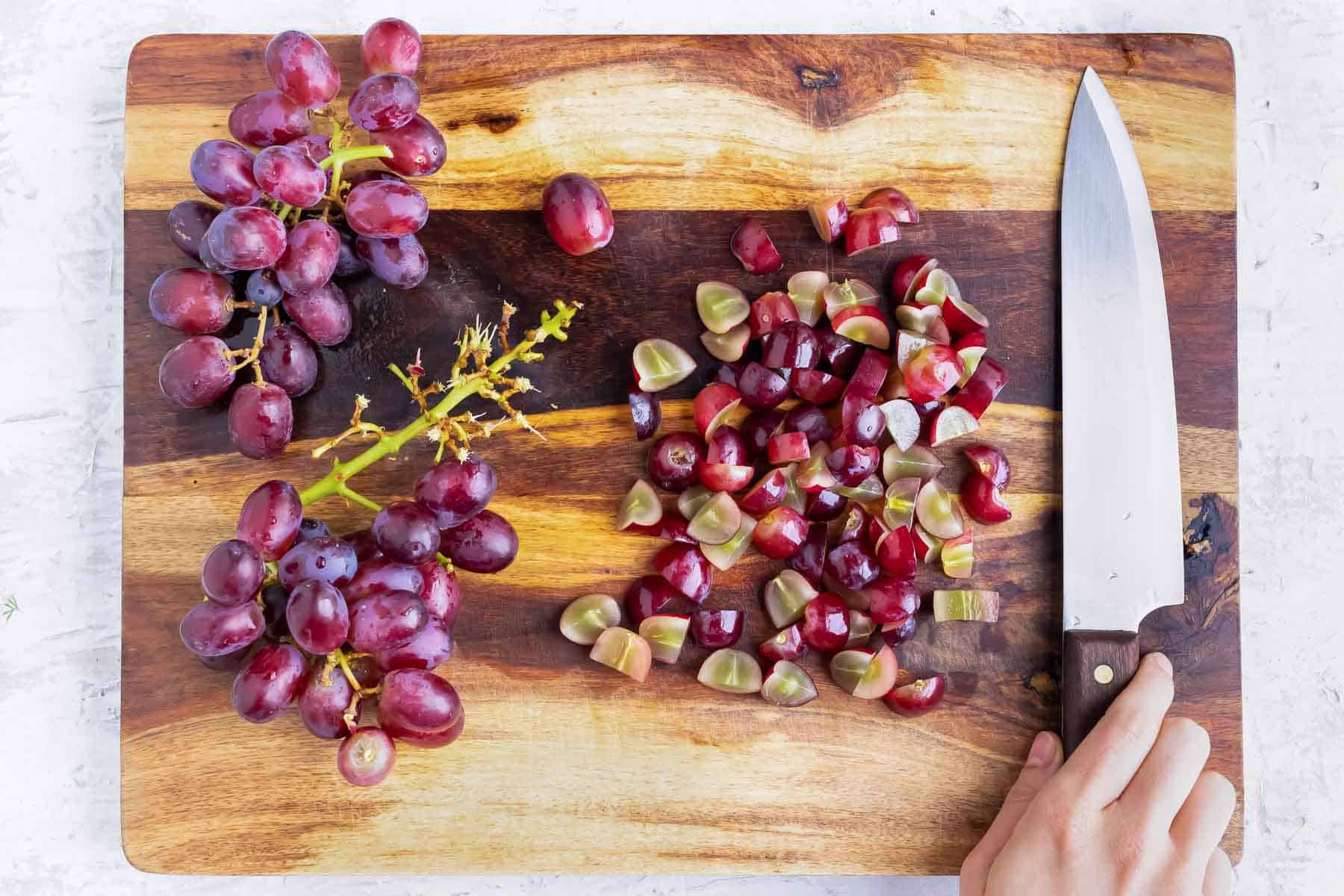 Grapes are sliced on a cutting baord.