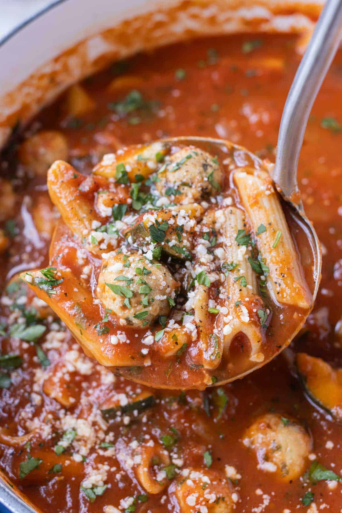 A ladle scoops out some Chicken Parmesan Meatball soup from a large pot.