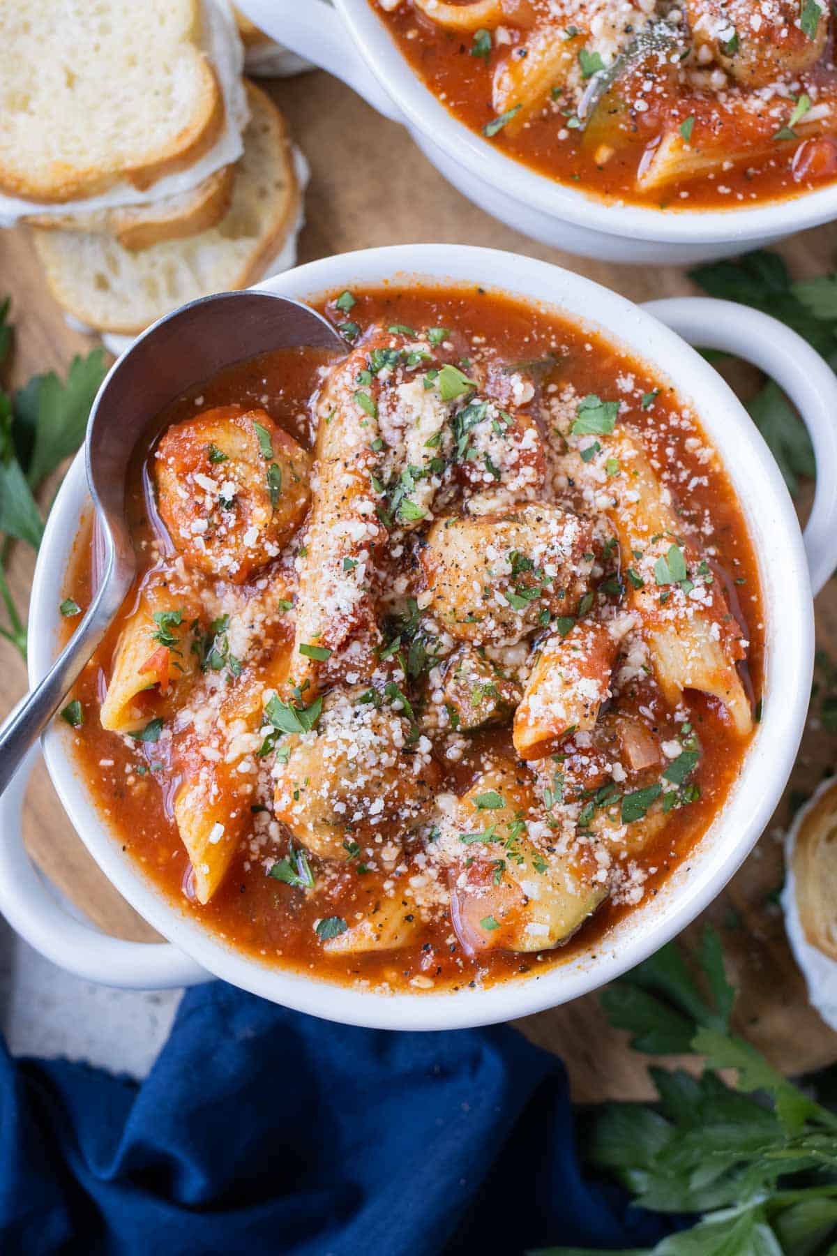 A white bowl full of Chicken Parmesan Meatball Soup with garlic butter cheese sandwiches surrounding it.